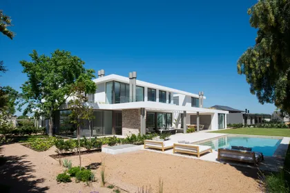 Casa moderna con piscina y jardín exuberante, fachada blanca — proyecto Casa AA, por Estudio Junor, en Pilar